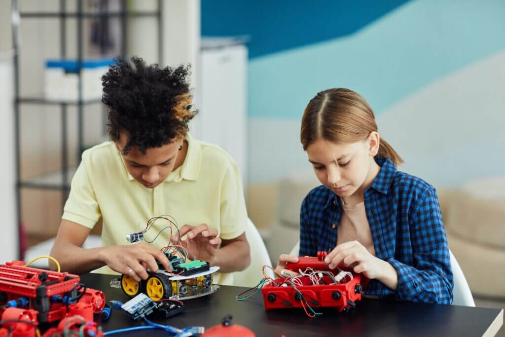 Two students work on robotic models at a shared work table.